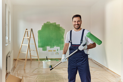 Happy male worker painting the wall in green color and looking at camera.